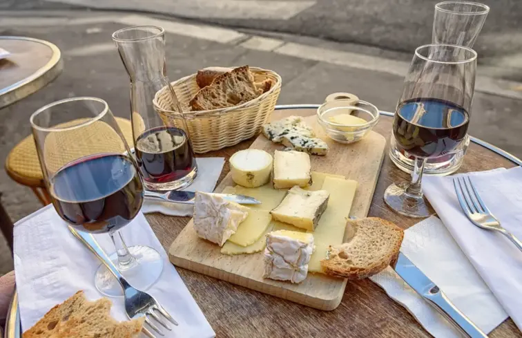 Uma mesa com queijos e copos de vinho, pão e toalhete.